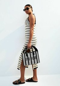 Abito a maglia a righe in bianco e nero, abbinato a sandali neri con zeppa e una borsa a righe con manici corti e dettagli testuali.