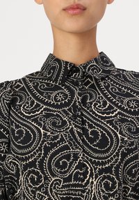Black button-up shirt featuring a cream paisley pattern, textured fabric, and a classic collar with five buttons.