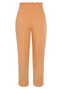 Růžové kalhoty barvy broskve s volánkovým pasem, sklady vpředu a manžetovým lemem. Vyrobeny z hladké, lehké látky.