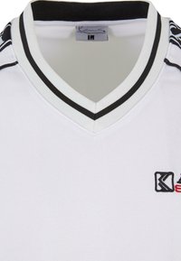 Balta polo marškinėlių su v-kaklu, juodai balta juostele ant apykaklės ir siuvinėtu logotipu. Sklandus audinys su reguliaraus prigludimo dizainu.