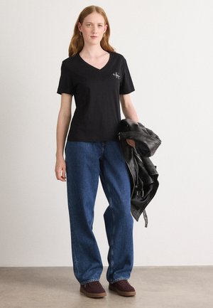 Zwarte V-hals t-shirt van katoen, gecombineerd met blauwe brede jeans en een zwarte leren jas, gedragen met bruine suède schoenen.