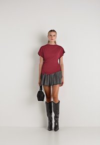 Maroonskortærmet top, grå plisseret mini-skirt, sorte knæhøje støvler og en lille sort håndtaske. Ensfarvede og moderne designfunktioner.