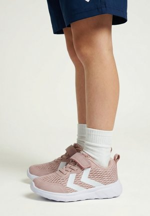 Kind trägt rosa Mesh-Sneakers mit weißen Chevron-Streifen, weiße Socken und marineblaue Shorts, steht auf hellem Hintergrund.