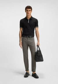 Czarna polo z szarymi akcentami, dopasowane jasnoszare spodnie, czarne lordsy i czarna torba w ręku; minimalistyczny design, casualowy wygląd.