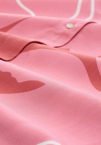 Chemise en tissu rose avec une texture lisse, présentant des motifs abstraits de rose clair et foncé, une fermeture à boutons et un col replié.