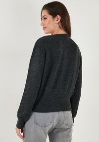 Dark gray knitted sweater with ribbed hem, round neckline, and long sleeves, featuring a soft texture and minimalistic design.