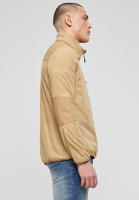 Hellbrauner Fleece-Pullover mit hohem Kragen, kontrastierenden hellbraunen Einsätzen an den Ärmeln und einem Reißverschluss am Hals.