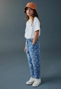 Blugi de denim cu buline albe mari, asortați cu un tricou alb simplu și o pălărie tip găleată portocalie, completați de adidași albi.