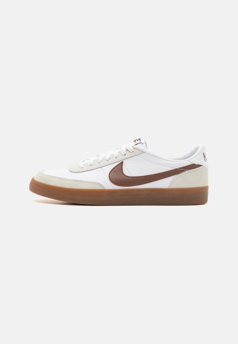 Baskets basses blanches avec le logo Nike en forme de virgule marron, accents en daim clair sur le bout et le talon, lacets blancs, et semelle en caoutchouc gum.