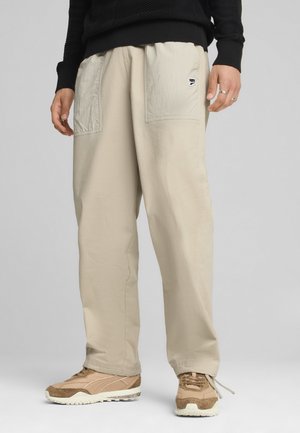 Beige Hose mit großen Fronttaschen, elastischem Bund und weichem Stoff. Kombiniert mit hellbraunen Sneakern mit strukturierten Akzenten.
