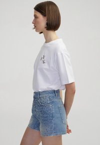Camiseta blanca de manga corta con piedras de strass decorativas y pantalones cortos de denim de tiro alto con diseño degradado y embellishments dispersos.