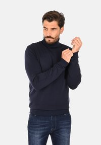 Maglione dolcevita blu navy realizzato in morbido materiale, con polsini e orlo a coste, abbinato a jeans di denim.