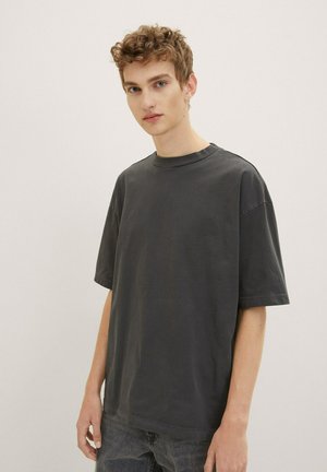 Dark gray cotton t-shirt with short sleeves and a crew neck. Features a relaxed fit and minimal stitching details. Worn with dark jeans.