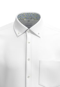 Camicia bianca con colletto a bottone, con un interno colletto a motivo floreale. Presenta una tasca sul lato sinistro e bottoni bianchi.