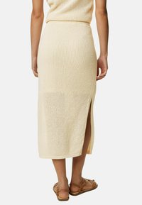 Strikket midi nederdel i lys beige med sideslid, der har en tekstureret vævning og en figursyet talje. Kombineret med brune flade sandaler.