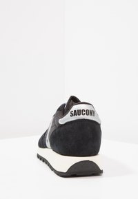 Svarta mockaskor för sport med grå detaljer, vit mellansula, gummiyttersula och "SAUCONY"-logotyp på hälen. Klassisk löpdesign.