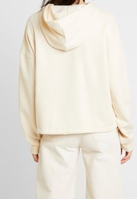 Krämsfärgad huvtröja med avslappnad passform, långa ärmar och ribbad nederkant. Materialet ser mjukt och något texturerat ut.