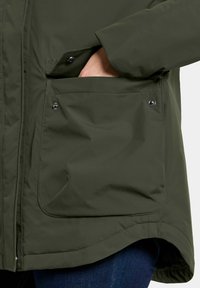 Groene waterdichte jas met een drukknoopzak en een soepele textuur, met een licht taps toelopende zoom en zonder zichtbare patronen.