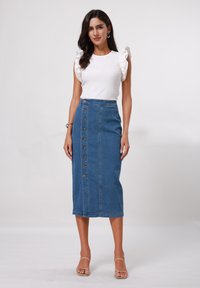 Vit ribbad topp med volangärmar, kombinerad med en högmidjad blå denimkjol med framknäppning och sidofickor.
