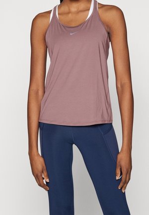 Kobieta ubrana w bezrękawnik sportowy w kolorze malwy z logo Nike oraz granatowe, dopasowane legginsy treningowe, stojąca na jednolitym tle.