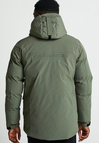 Olīvu zaļš izolēts mētelis ar kapuci. Strukturēta auduma, regulējamas aproces un aizmugures ventilācijas detaļa. Priekšā pilna garuma rāvējslēdzis.