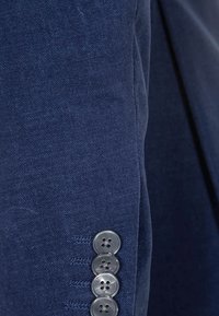 Gros plan sur la manche d'un blazer bleu marine avec quatre boutons gris alignés verticalement près du poignet.