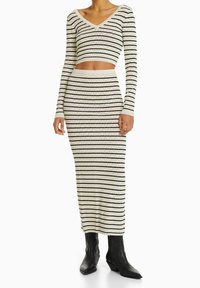 Stickad tvådelad set bestående av en croptop med långa ärmar och V-ringning, tillsammans med en midilång kjol, i krämfärg med svarta ränder och triangelmönster.