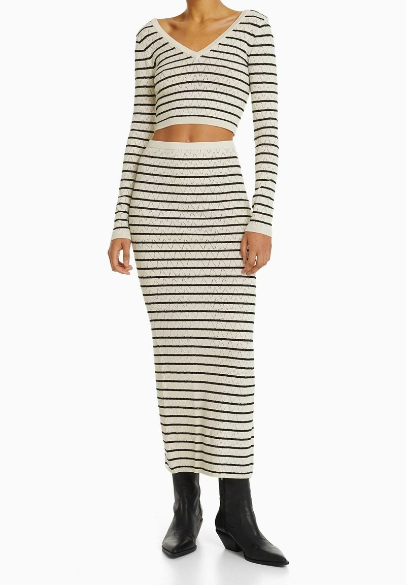 Stickad tvådelad set bestående av en croptop med långa ärmar och V-ringning, tillsammans med en midilång kjol, i krämfärg med svarta ränder och triangelmönster.