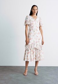 Abito midi floreale con scollatura a V, maniche a volant e orlo a strati. Morbido misto cotone in colori pastello rosa, crema e verde. Tacchi trasparenti con cinturini.