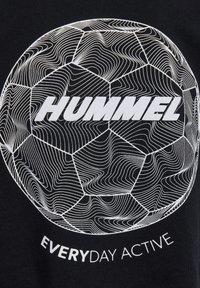 Svart bomullströja med en vit grafisk bild av en fotboll med vågiga linjer, som visar texten "HUMMEL" och "EVERYDAY ACTIVE".