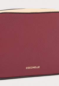 Pochette cosmetica in pelle bordeaux con finitura testurizzata, logo dorato e bordo superiore crema a contrasto con rifiniture nere.