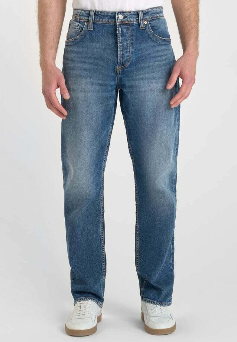 Jean en denim bleu clair avec une coupe droite, décoloration à l'avant, design à cinq poches et détails de couture subtils, associés à des baskets blanches.