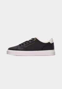 Baskets basses noires avec semelle blanche et col de talon, lacets noirs et logo doré "Tommy Hilfiger" sur le côté.