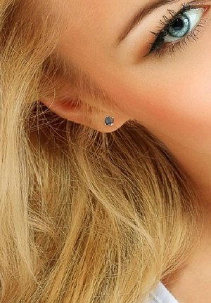 Boucle d'oreille en argent avec une pierre précieuse noire géométrique, mise en valeur contre des cheveux blonds, présentant une finition polie et un design minimaliste.