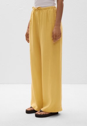 Pantalons larges jaunes en tissu léger avec une taille élastique et un cordon de serrage. Présente une texture lisse et une coupe décontractée.