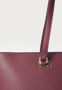 Bordeaux leren handtas met een gestructureerd oppervlak, voorzien van een gouden hardware accent en een enkele schouderriem.