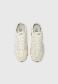 Kremfargede New Balance-sko med hvite lisser og et teksturert design, sett fra oven mot en hvit bakgrunn.