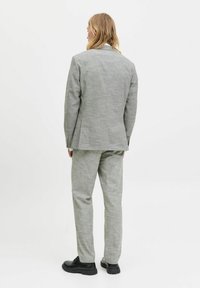Traje texturizado de color gris claro con chaqueta ajustada y pantalones a juego, combinado con zapatos negros de cordones. Vista desde atrás.
