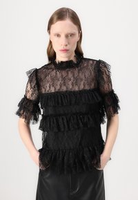 Top in pizzo nero con rouches sovrapposte, tessuto trasparente e maniche corte con rouches. Collo alto con delicati dettagli arricciati.