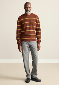 Brown striped sweater with gray and yellow lines, paired with gray jeans and black shoes. The fabric appears knitted and textured.