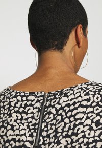 Haut à motif noir et blanc avec un col rond et un détail de fermeture éclair au dos ; présente un tissu texturé et des manches courtes.