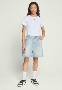White cotton t-shirt with black logo, paired with light blue denim shorts, and black and white sneakers with white socks.