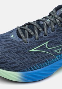 Αθλητικό παπούτσι με ανώτερο ύφασμα από ναυτικό πλέγμα με πράσινες λεπτομέρειες, υφασμάτινη επιφάνεια και πέλμα σε γκρι-γαλάζιο και πράσινο χρώμα, σχεδιασμένο για απόδοση.