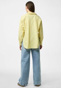 Camicia a maniche lunghe giallo a strisce con vestibilità ampia. Il retro presenta un orlo curvo e polsini con bottoni, abbinata a jeans a gamba larga di un blu chiaro.