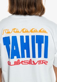 White t-shirt featuring bold blue "TAHITI" text and red "Quiksilver" logo, with a wave graphic in orange across the top.