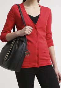 Röd cardigan med v-ringning, långa ärmar och knäppning med knappar. Matchas med en svart läderväska med kedjeaccent och logocharm.