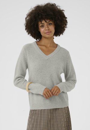 Helles graues V-Ausschnitt-Pullover aus weichem Strickstoff, mit langen Ärmeln und gerippten Bündchen, kombiniert mit einem karierten Rock.