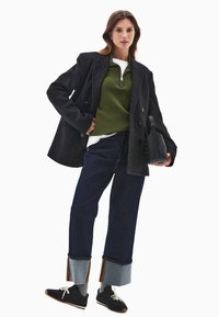 Mustapeitukka takki, vihreä neule, valkoinen paita, tummat lyhyet farkut farkkukuvioilla ja mustat tennarit valkoisilla nauhoilla. Musta käsilaukku.