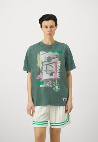 Groene oversized t-shirt met gedurfde grafische print, korte mouwen en ronde hals. Gecombineerd met witte gestreepte shorts met groene accenten.