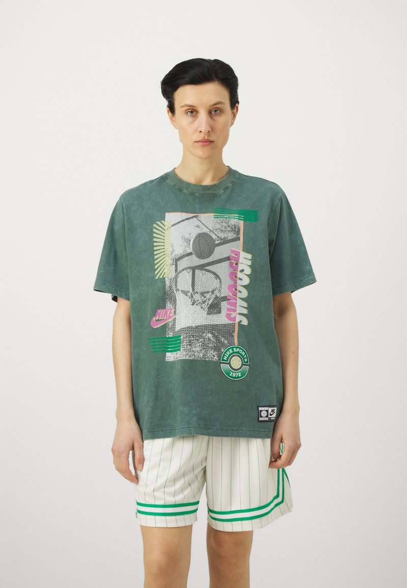Groene oversized t-shirt met gedurfde grafische print, korte mouwen en ronde hals. Gecombineerd met witte gestreepte shorts met groene accenten.